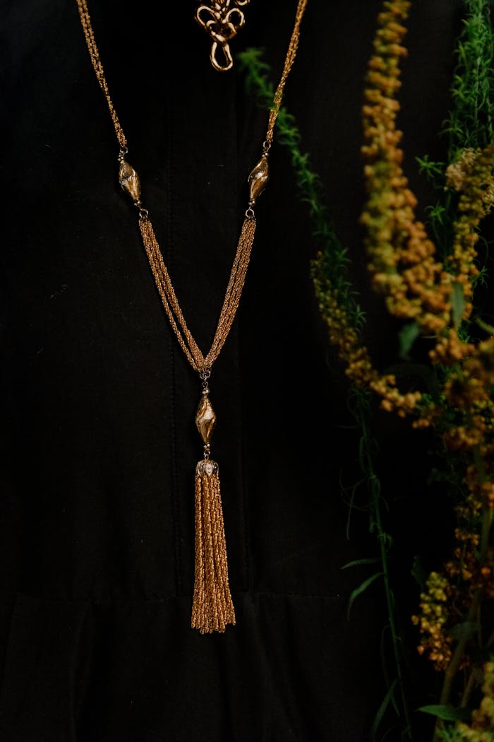 contact-img An elegant gold necklace against a black background with greenery accentuating luxury.