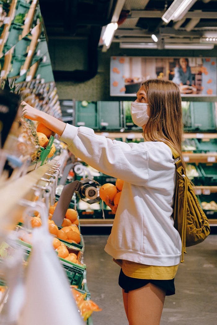 hero-img-01 Woman wearing mask choosing oranges in a supermarket during the pandemic.