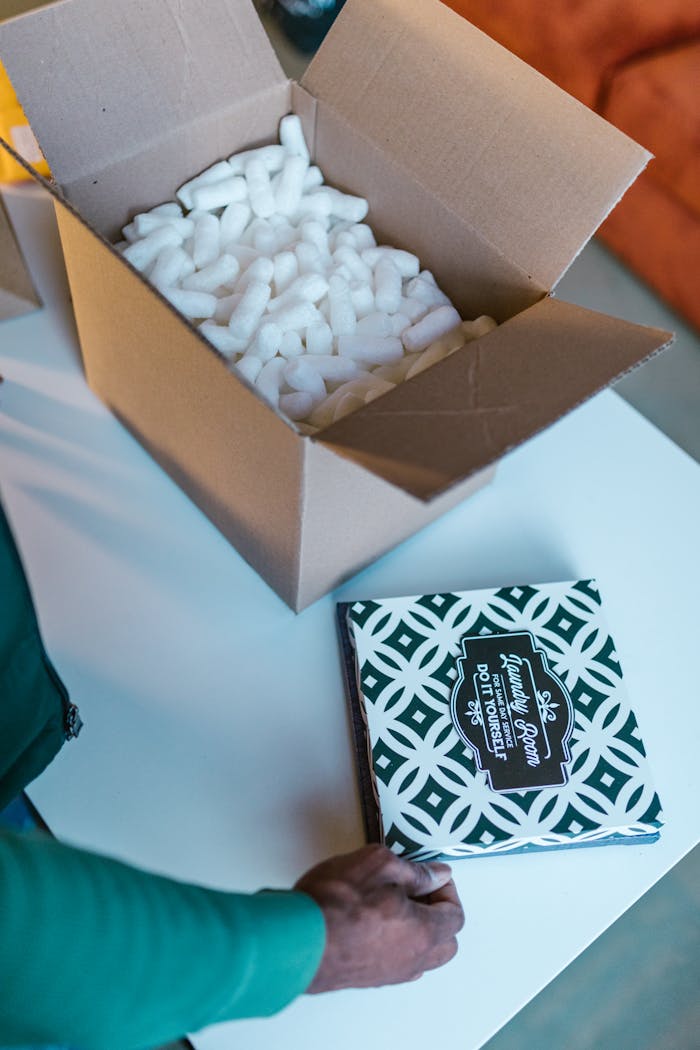 gallery-5 Open cardboard box with packing peanuts and hand placing patterned item.